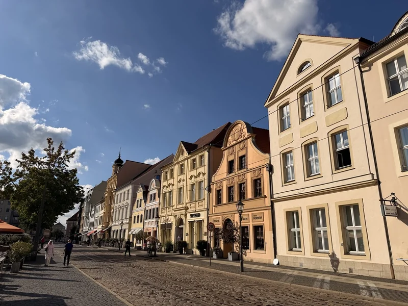 Renovierte Häuser am Altmarkt in Cottbus unter blauem Himmel, mit Menschen auf dem Platz.